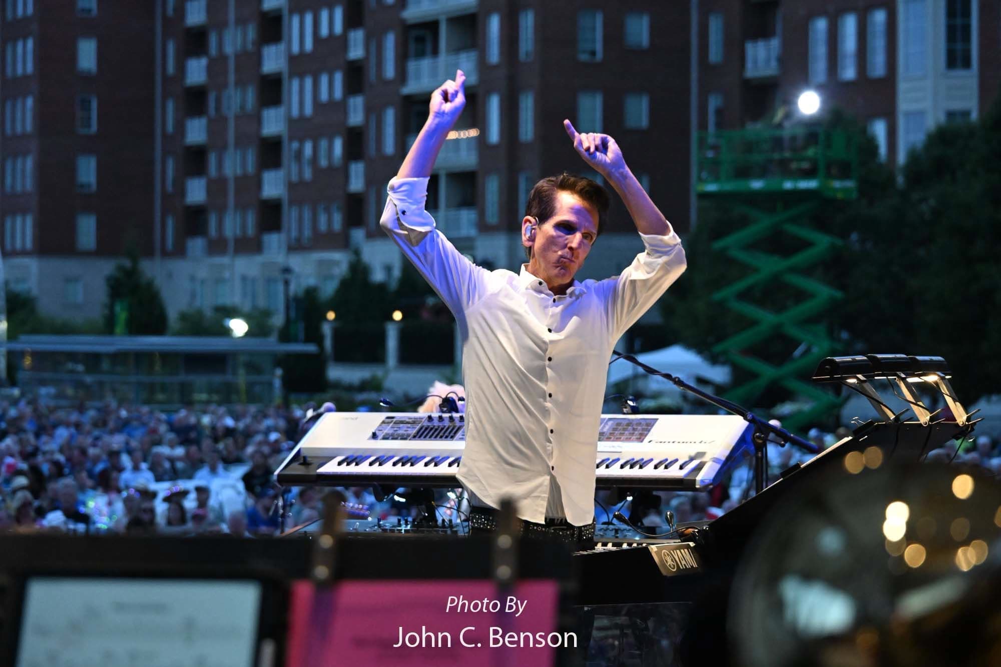 Tom Brooks conducting with both arms raised on the downbeat, audience behind him