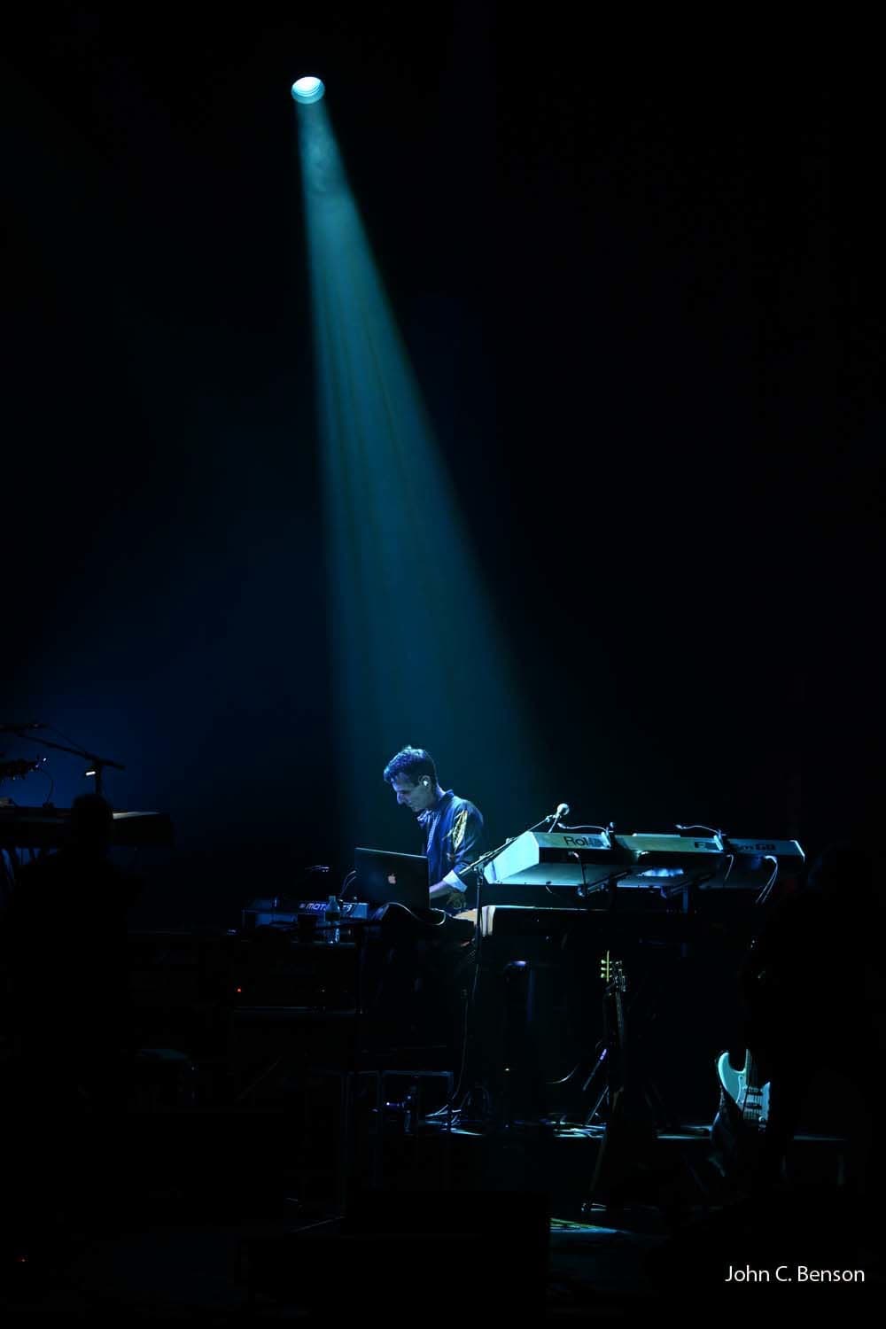 Tom Brooks lit by a single spotlight at his keyboard rig in a darkened hall